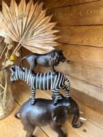Dekoobjekt aus dunklem Holz aus gestapelten Tieren: Elefant, Zebra, Löwe, im Hintergrund trockenblumen