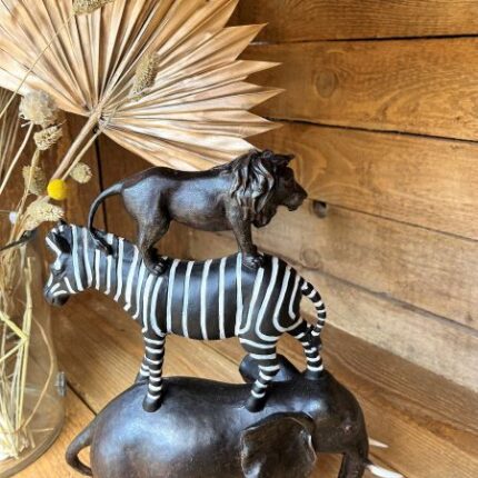 Dekoobjekt aus dunklem Holz aus gestapelten Tieren: Elefant, Zebra, Löwe, im Hintergrund trockenblumen